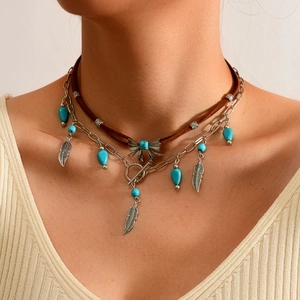 Detail van een bohemian gelaagde ketting met leren koord, turquoise kralen en een veerhanger