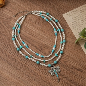 Close-up of bohemian layered pearl and turquoise necklace with vintage dragonfly pendant