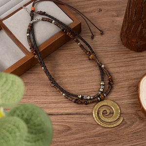 Détail d'un collier bohème double épaisseur avec pendentif spirale sur bois rustique