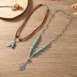 Detail van een boho-halsketting set met turkoois kralen, zilveren veer en zonnebloem hanger