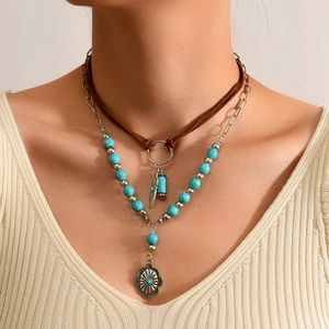 Detail van gelaagde ketting met turkoois, zilveren veer en bohemien bloemhanger