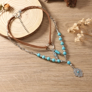 Macro-opname van dubbellaagse boho-ketting met turquoise kralen en veerhangers