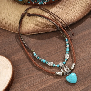 Detail of bohemian layered necklace featuring a turquoise heart pendant and metal feathers