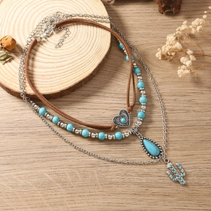 Detail van gelaagde turkoois ketting met cactus- en hartbedels op houten achtergrond