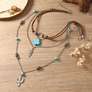 Detail van gelaagde bohemian ketting met turquoise cactus en kruis hangers op hout