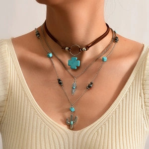Detail van een boho gelaagde kettingset met turkoois kruis, veer en cactus hangers