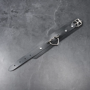 Detail of black punk leather choker featuring a silver heart ring and adjustable buckle