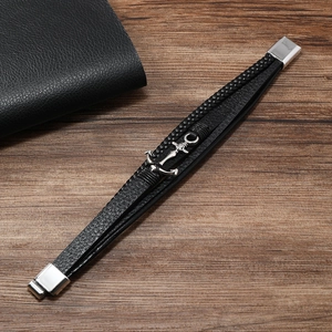 Detail of multi-layer braided leather bracelet with silver anchor charm on wooden table