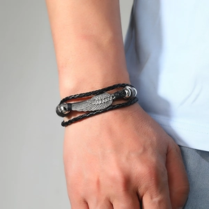 Close-up of braided leather bracelet featuring a silver alloy wing charm and vintage beads