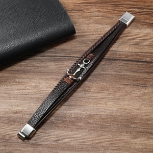 Detailed view of multilayer leather bracelet with silver anchor charm on a wooden desk