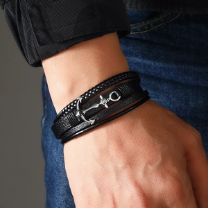 Macro view of men's multi-layer leather bracelet with silver anchor and skull charm