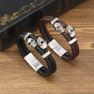 Détail de bracelets en cuir tressé avec crânes argentés et fermoir magnétique style punk