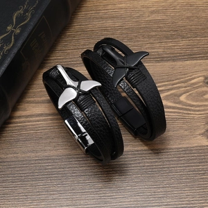 Detail view of multi-layer leather bracelets with silver whale tail charms on wood