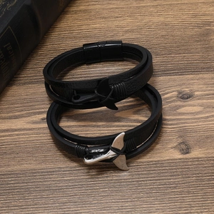 Men's layered leather bracelets with whale tail charms and magnetic clasps on wood table
