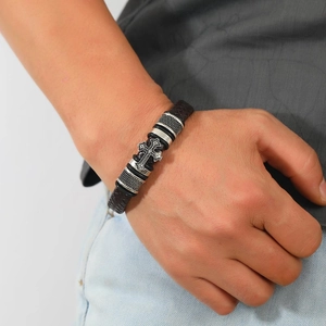 Men's woven leather bracelet with silver cross charm worn on wrist in a casual setting