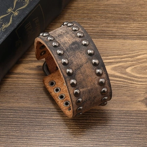 Macro shot of wide brown leather bracelet with vintage metal rivets on wooden table