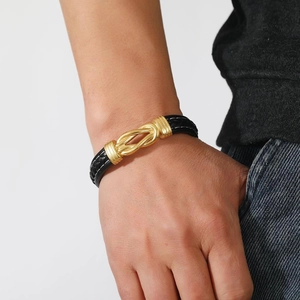 Detail of black braided leather bracelet with gold horseshoe buckle on wrist