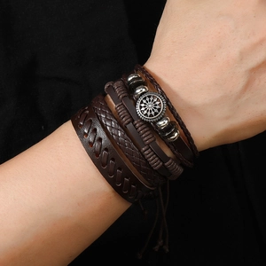 Detail of layered brown braided leather bracelet with vintage metal badge and beads