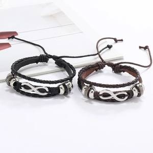 Détail de bracelets en cuir tressé noir et marron avec breloques infini argentées ajustables
