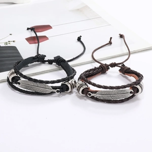 Détail de bracelets en cuir tressé avec pendentifs plume argent et nœuds réglables