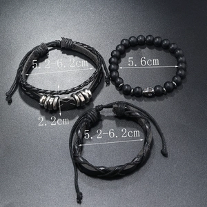 Macro detail of men's matte black beaded skull bracelet and woven leather band set