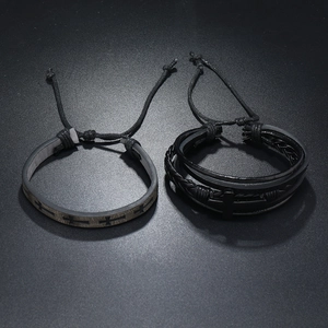 Detail of two men's black leather cross bracelets with woven cords and metal charms