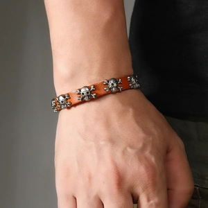Detail of orange leather punk bracelet with silver skull charms on male wrist