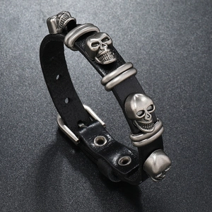 Detail of black punk leather bracelet featuring three silver metal skull charms and buckle
