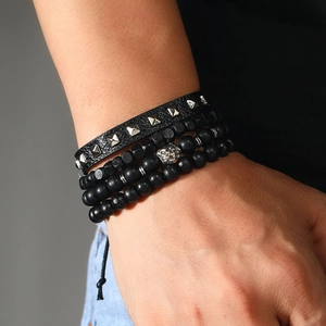 Detail of men's layered black bead bracelets featuring a silver lion head charm and studs