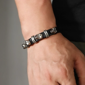 Close-up of punk leather bracelet featuring vintage silver skull charms and rivet buckles