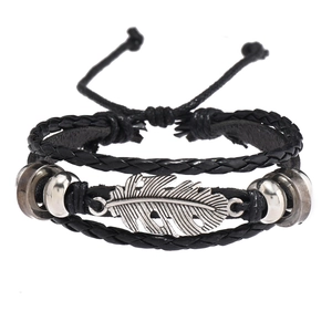 Détail d'un bracelet multicouche en cuir noir avec pendentif plume en métal argenté