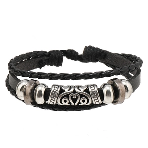 Détail d'un bracelet multicouche en cuir tressé avec breloque cœur et perles argentées