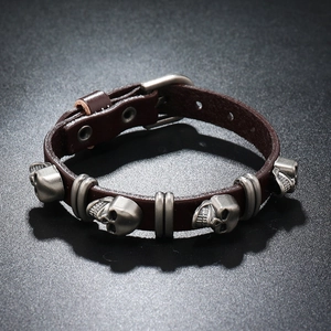 Detail of dark brown leather punk bracelet with silver skull charms and buckle strap
