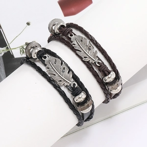 Détail de bracelets multicouches en cuir avec breloques plumes vintage en noir et marron