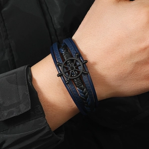 Macro detail of men's leather braided bracelet with a matte black nautical helm charm