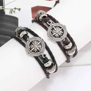 Vue détaillée des breloques boussole vintage et des bracelets en cuir tressé multicouches