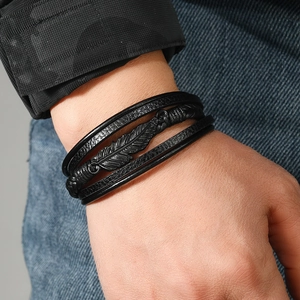Détail d'un bracelet multicouche en cuir pour homme avec un pendentif plume noire en métal