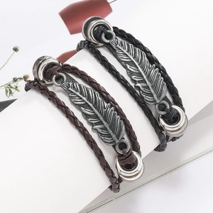 Détail de bracelets multicouches en cuir tressé avec breloque plume en argent antique