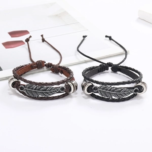 Détail de bracelets en cuir avec pendentifs plumes en métal et cordons tressés réglables