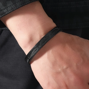 Close-up of black feather-textured open cuff bracelet worn on male wrist with denim jacket