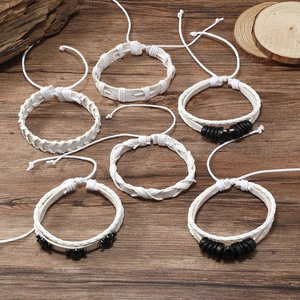 Detailweergave van zes gevlochten leren herenarmbanden met doodshoofd en kralen op hout