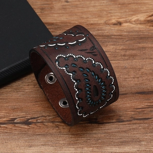 Brown leather cuff bracelet with paisley pattern and metal snap buttons on wood background