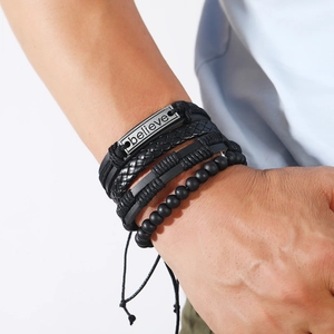 Dettaglio di bracciali multistrato da uomo in pelle nera con placca Believe e perline