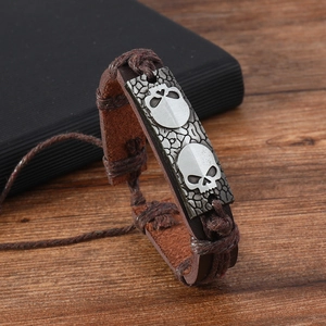 Gros plan d'un bracelet en cuir tressé marron avec des breloques crâne en alliage argenté