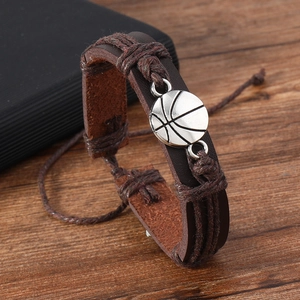 Close-up of men's leather woven bracelet with silver basketball charm on wood background