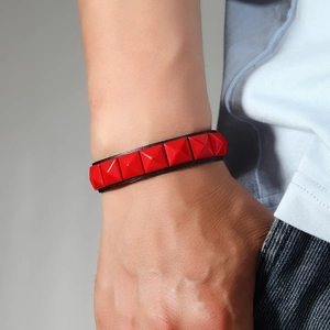 Bracelet punk avec clous pyramides rouges sur bande de cuir noir porté par un mannequin