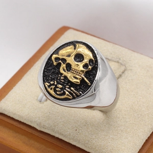 Macro shot of silver ring with gold pirate skull emblem on black textured surface