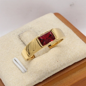 Anillo de acero de titanio dorado con gema roja rectangular en soporte de exhibición