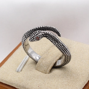 Vintage silver snake ring with scale texture and red crystal eyes on a jewelry stand