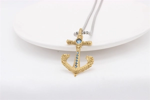 Detailed shot of a vintage gold anchor pendant with blue gemstones and a silver chain